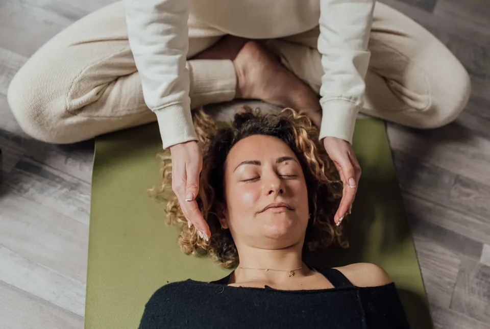 A person lying comfortably with eyes closed while a practitioner guides a relaxation session.