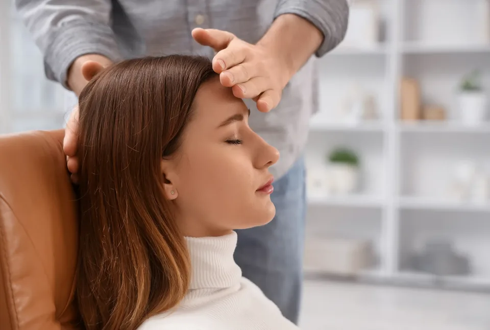 A client rests back in a chair with her eyes closed while a practitioner guides a calm session.