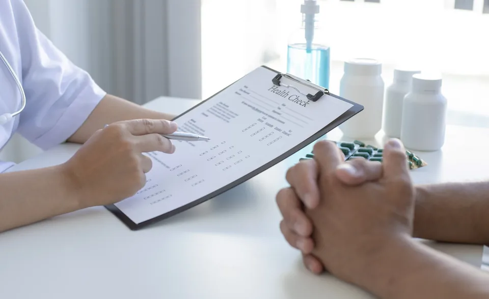 A practitioner reviewing written notes on a clipboard with a person seated opposite at a table.